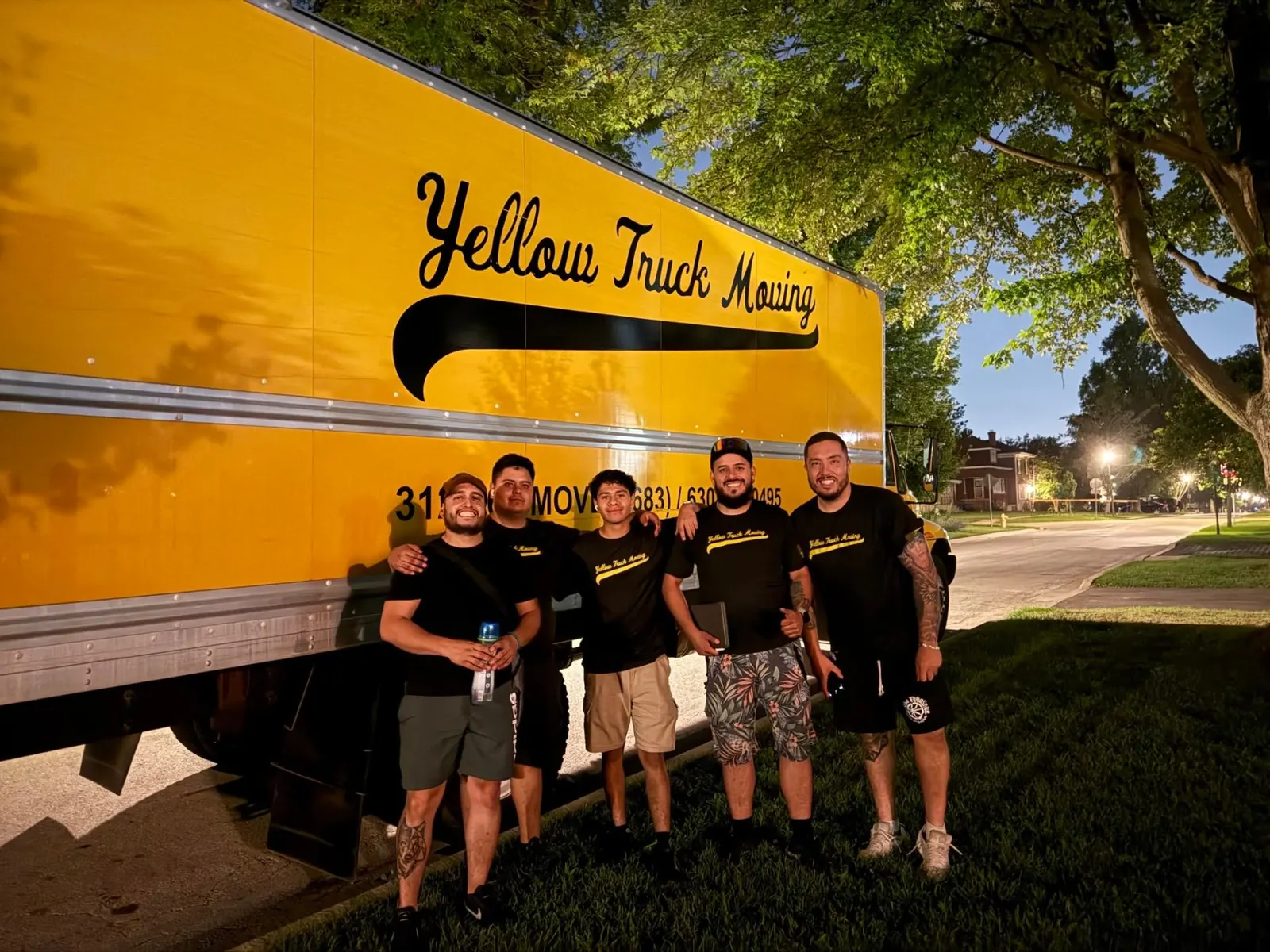 Yellow Truck Moving team of five posing in front of a yellow moving truck at dusk